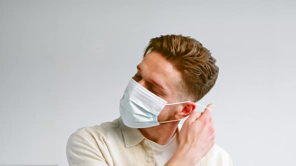 Experienced male model with beard takes off blue disposable face mask alt