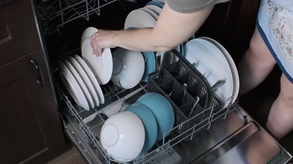 Woman in Apron Putting Dishes Into Dishwasher alt