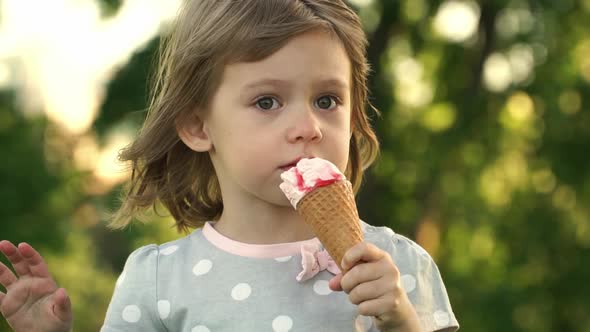 Child Girl Eats Strawberry Ice Cream at Sunset on Background of Trees in Summer Park