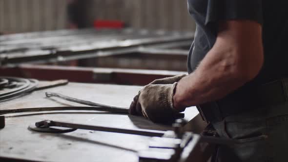 Master Bends Metal Bar in Vice on Workplace for Manufacture of Metal Structures alt