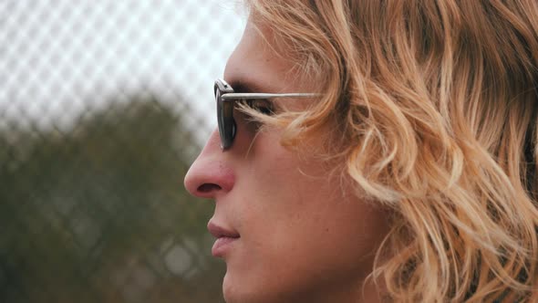 portrait of a handsome confident young man with sunglasses and long blond hair. Side view