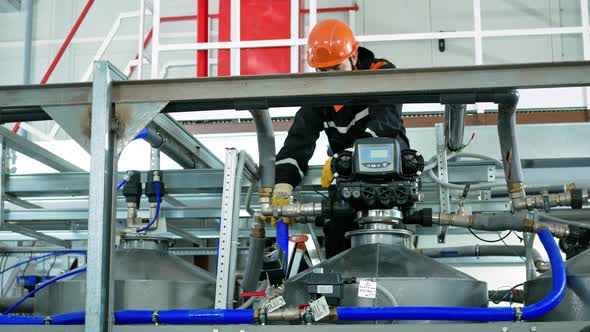 A Worker Wearing a Helmet and Gloves Untwists the Pipes for Dismantling the Distribution Unit to alt