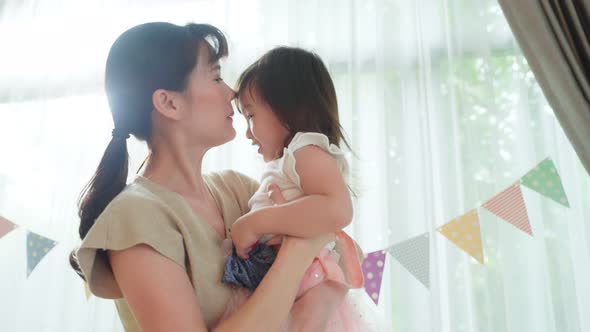 Asian beautiful loving mother hold little baby girl daughter in arm and spinning around in house. alt