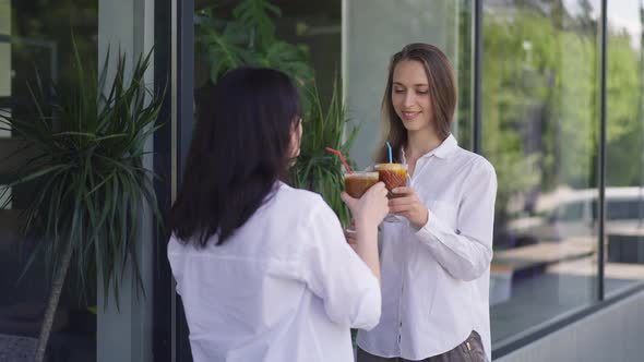 Positive Young Women Standing on City Street Drinking Cocktails in Slow Motion Smiling alt