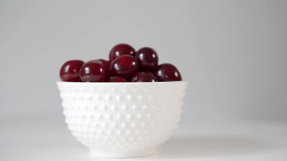 A Rotating Bowl With Red Fresh Ripe Cherries On The Background Of A White Wall