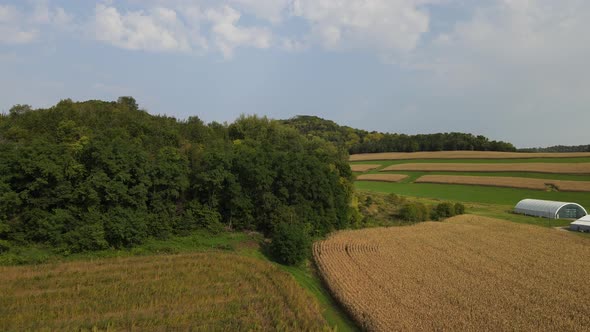 Flyvover of farm field in valley with bluffs. Trees along the side of bluff. Dirt road.