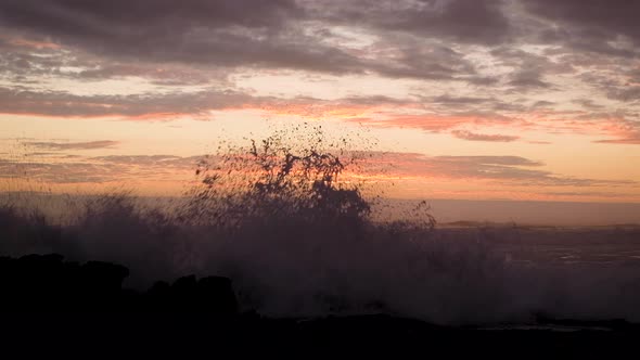 Rough Atlantic ocean waves crashing against rocky shore with orange sunset alt