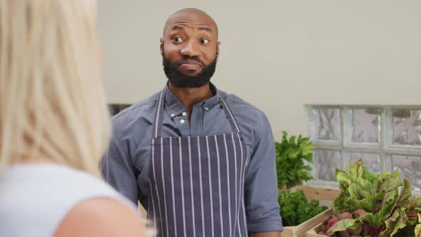 Video of happy african american salesman showing organic vegetables to caucasian female customer alt