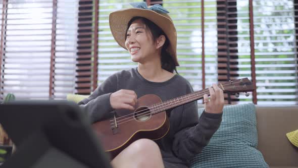 asian female online learning playing ukulele on couch sofa at living room