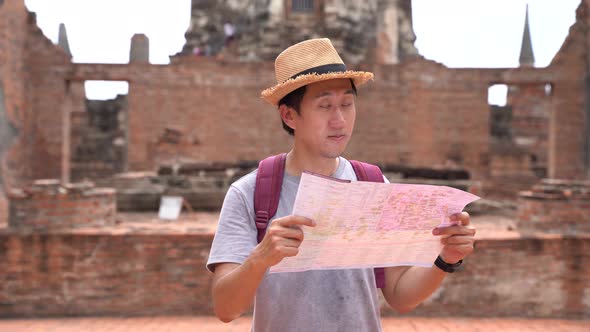 Young Asian Man with Hat Looking at Map in Traditional Temple in Ayutthaya Historic Park Thailand alt