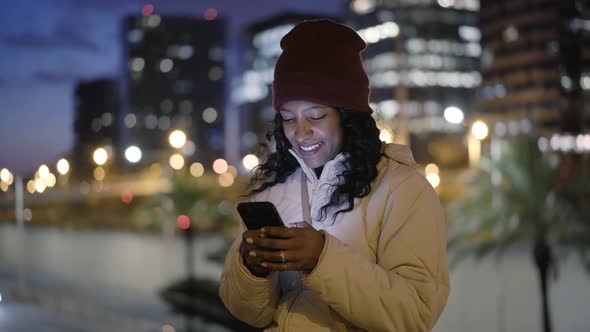 The Girl with Her Face Illuminated By the Light of the Mobile Phone Screen is Using the Smart Phone alt