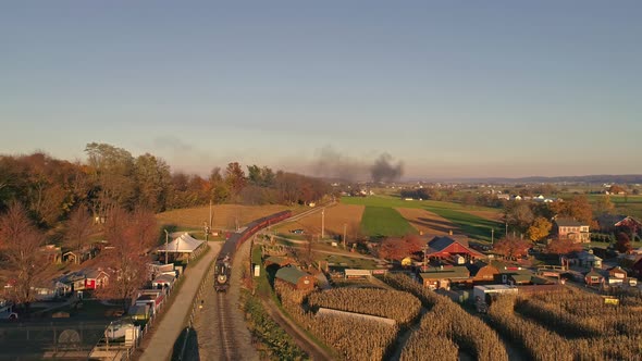 Aerial View of an Antique Steam Locomotive Approaching Pulling Passenger Cars and Blowing Smoke and Steam During the Golden Hour in late Afternoon alt