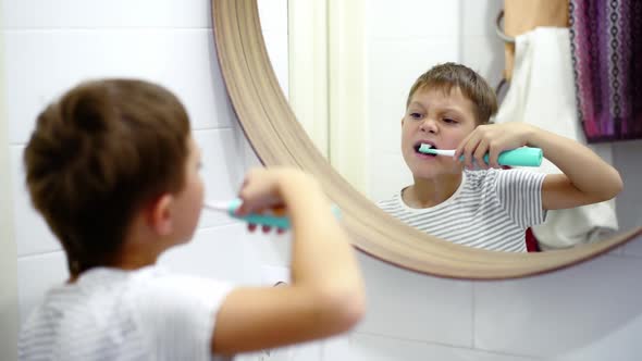 Cute Caucasian Boy Brushing His Teeth with Electric Brush Looking in the Mirror