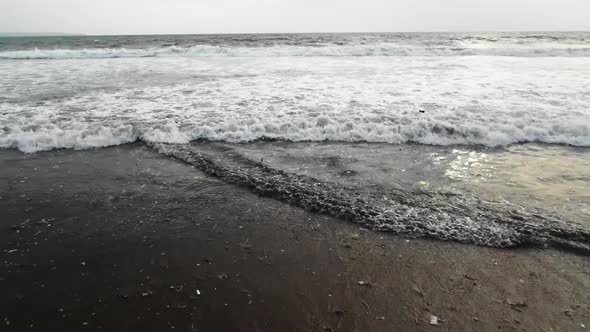 Pull back shot at the beach, as the ocean is full with trash, waves washing out plastic to the shore alt