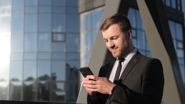 Happy Businessman Holding a Smartphone and Laughing alt