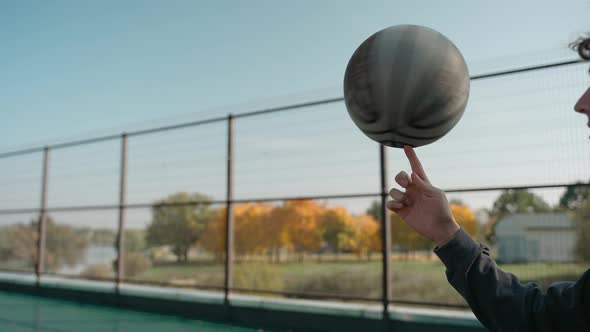 Boy Stands on a Basketball Court and Spins a Ball on His Finger on a Sunny Day