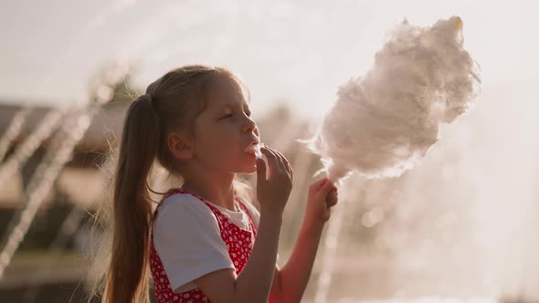 Girl Puts Cotton Candy in Mouth and Looks at Sticky Fingers alt