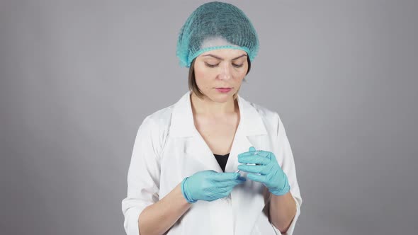 Young Female Doctor in Gloves Holding a Syringe and Preparing Injection Isolated on Grey Background alt