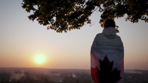A Woman Stand with the Flag of Canada Against a Clear Sky at Sunset alt