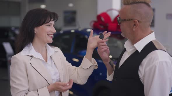 Female Car Dealer Passing Keys to Satisfied Male Buyer in Dealership Smiling alt