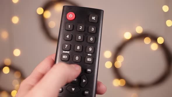 TV Remote Control Closeup Fingers Press Buttons Boke and Christmas Lights on a Blury Background