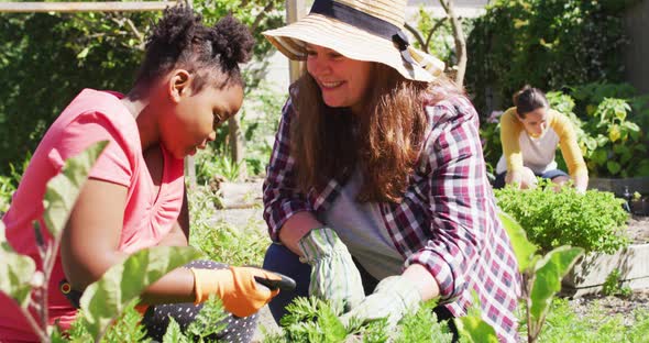 Happy caucasian lesbian couple and their african american daughter gardening together alt