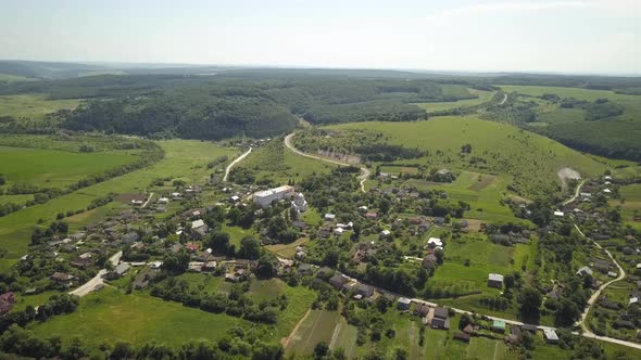 Aerial view of small village with small houses among green trees with farm fields and distant  alt