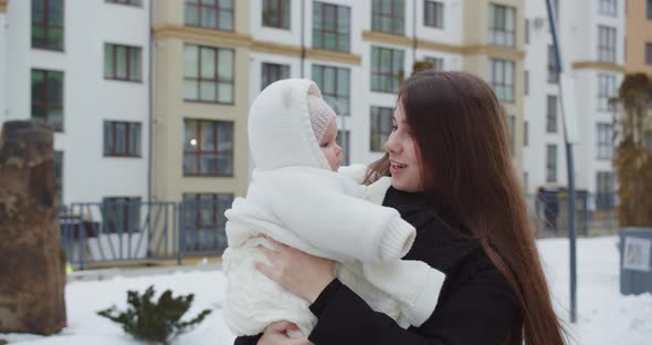 In Winter, A Mother Walks Down The Street With A Child In Her Arms
