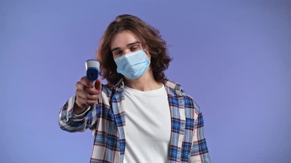 Man in Protective Mask Directs Electronic Noncontact Thermometer Into Camera Lens and Measures alt