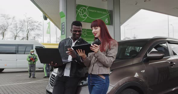 Young American Man Together With A Young European Girl Leaning On A Car Working alt