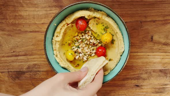 A Woman's Hand Scoops Up a Piece of Bread Delicious Hummus with Cherry Tomatoes and Pine Nuts with