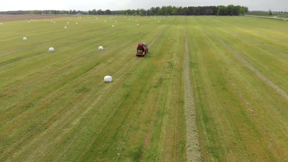 A Red Tractor Collects Hay and Presses It Into White Bales Using a Baler, Shot From Above alt