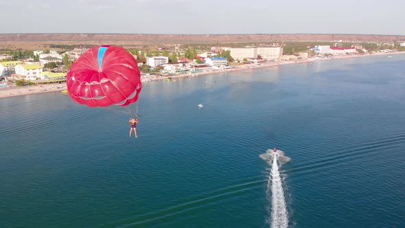 Towing Red Parachute Behind a Jetski Over the Sea Along the Beach at Sunset alt