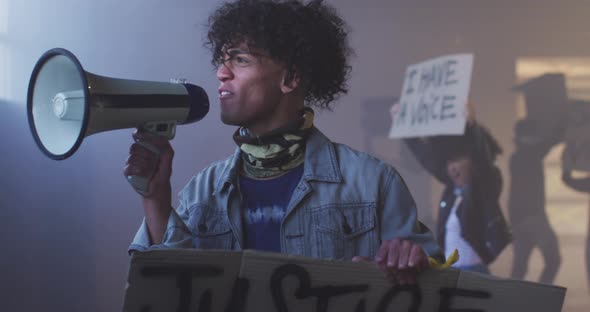 Diverse group of people wearing face masks holding protest signs shouting into megaphone alt