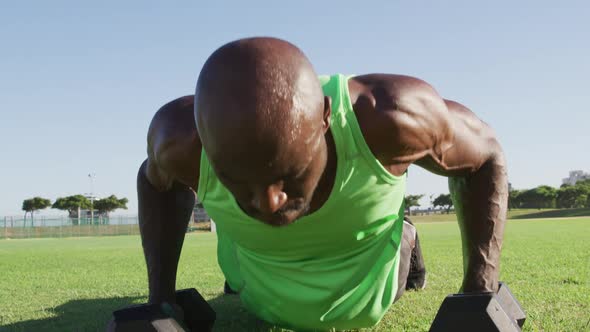 Tired african american man exercising outdoors doing press ups and lifting dumbbells alt