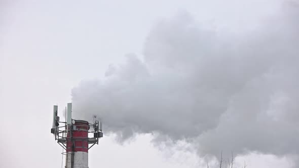 Thermal Power Station Pipe at Winter with Outgoing Smoke Steam and Isicles on Telecommunication