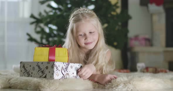 Close-up of Cute Caucasian Girl with Grey Eyes in Crown Lying at the Background of Christmas Tree alt