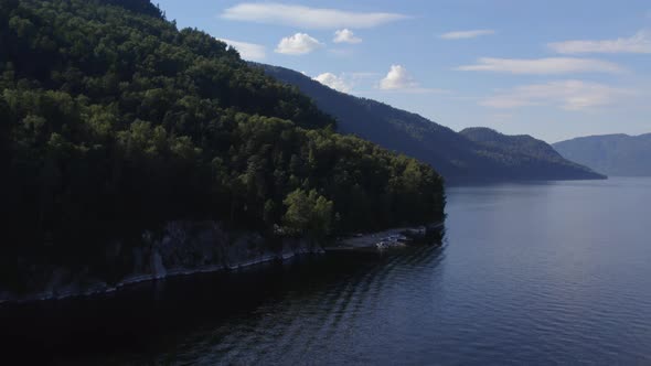Coastline of lake Teletskoye with forest and blue clear sky in Altai