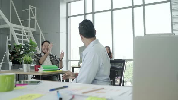 Asian creative businessman and his colleagues arms raised celebrating success at office alt