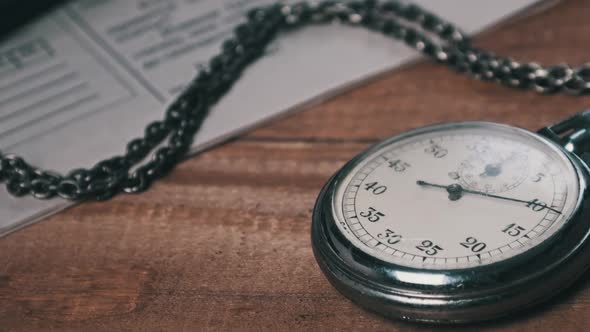 Vintage Stopwatch Lies on Wooden Desk with Old Documents and Counts Seconds alt
