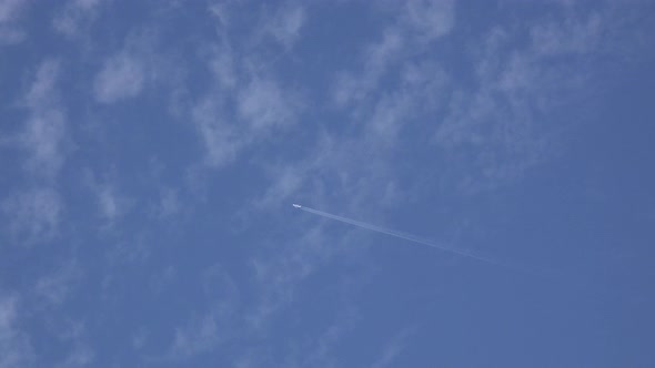 An airplane flies across a blue sky with white clouds.