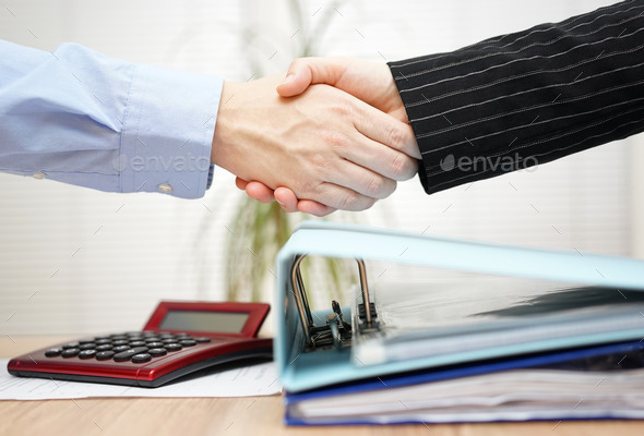 businessman and businesswoman are handshaking over binders