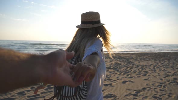 Beautiful Girl in Shirt with Backpack Holding Male Hand and Running on Empty Beach alt