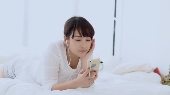 Young asian woman lying happy earphone listening music with relax and enjoy in the bedroom. alt