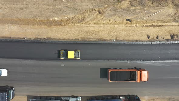 Aerial Shot of Roller Laying New Asphalt Layer and Trucks Standing at Roadside alt
