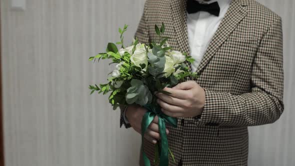 Groom with Wedding Bouquet in His Hands at Home. White Shirt, Jacket. Close-up Shot. Slow Motion alt