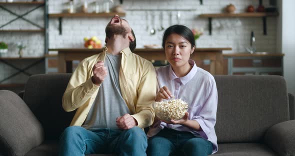 Young People Watching Comedy Movie on TV with Popcorn Sitting on Couch in Apartment alt