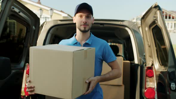 Portrait of Delivery Guy Taking Cardboard Box From Van and Carrying It to Customer's House alt