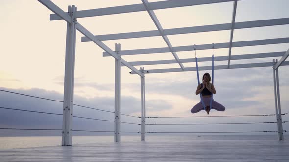 Woman Does Yoga Exercises Hanging on Slings on Empty Pier