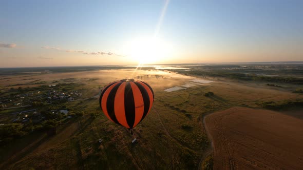Orange Hot air ballon floating above fields at beautiful sunrise